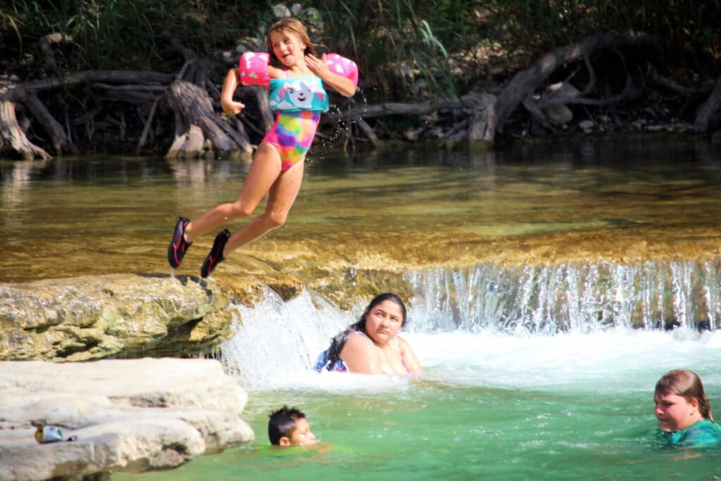 girl with water wings on  jumping into the Frio River 
